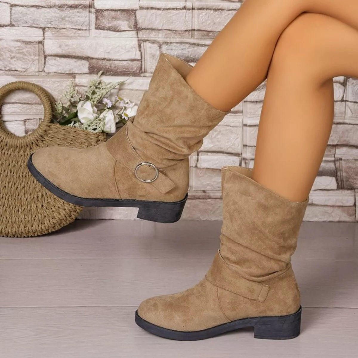 Tan knee-high boots worn by a person with a stone wall and woven bag in the background - Fashlot