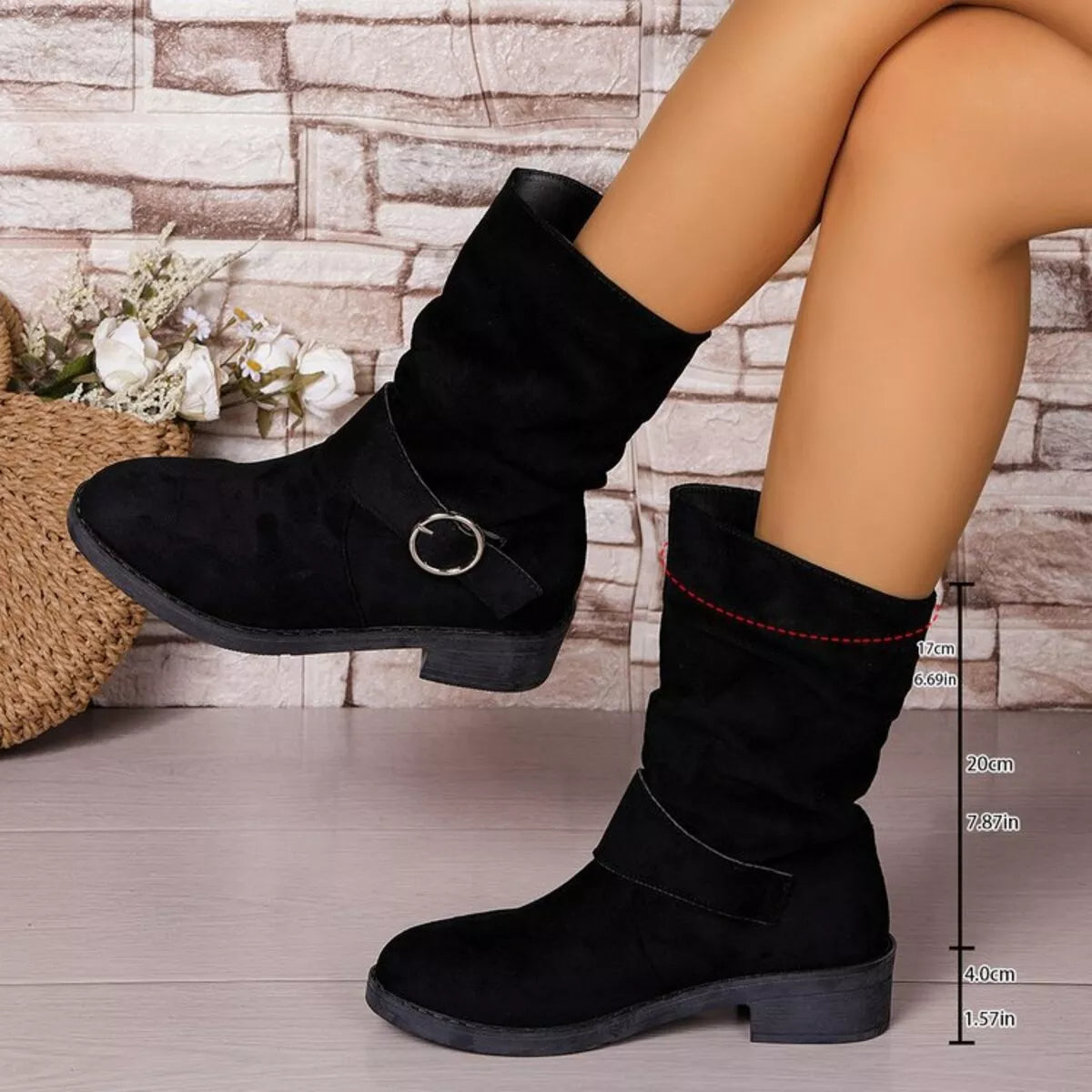 Black suede boots worn by a person with a stone wall background - Fashlot
