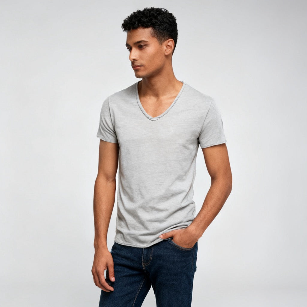 A man wearing a light gray v-neck t-shirt and dark blue jeans, standing against a light gray studio background.  - Fashlot
