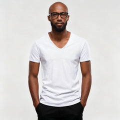 A man wearing a plain white short-sleeve V-neck t-shirt and black pants, standing against a light gray studio background. - Fashlot