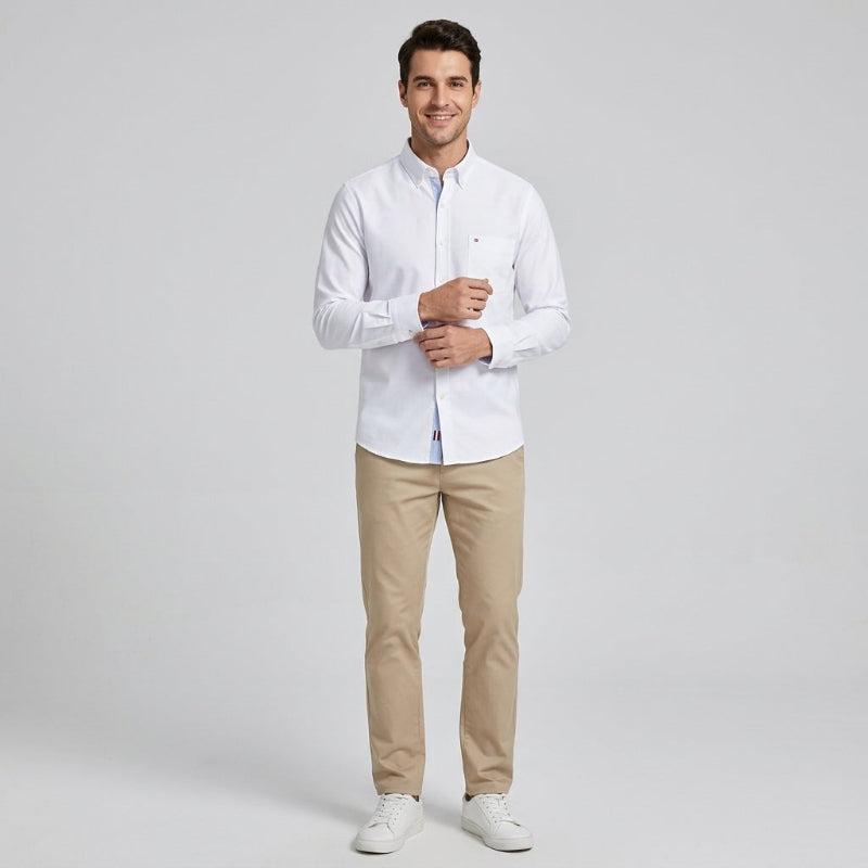A man modeling a white long-sleeve button-down shirt, paired with beige trousers and white sneakers, standing against a light gray studio background. - Fashlot