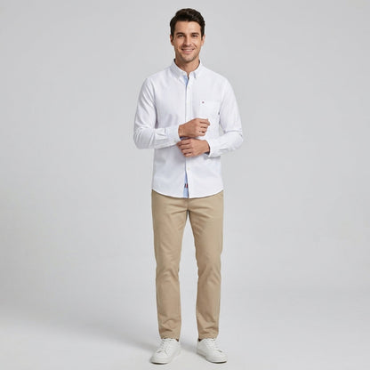 A man modeling a white long-sleeve button-down shirt, paired with beige trousers and white sneakers, standing against a light gray studio background. - Fashlot