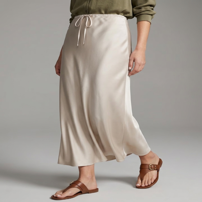 A model wearing a high-waisted, floor-length cream satin midi skirt with a drawstring waist, styled with an olive green top and brown leather sandals against a neutral gray studio background. - Fashlot