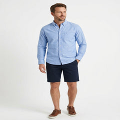 A man modeling a light blue long-sleeve button-down shirt paired with dark navy shorts and brown leather sneakers, standing against a plain white studio background. - Fashlot