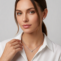 A woman wearing a delicate silver necklace with a small clear stone pendant and a matching silver stud earring, photographed against a soft light gray studio background. - Fashlot
