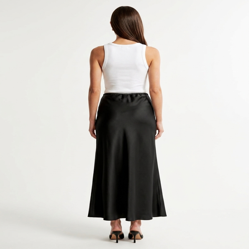 A woman shown from the back wearing a white sleeveless top and a long black satin-like skirt, standing against a plain light gray studio background. - Fashlot