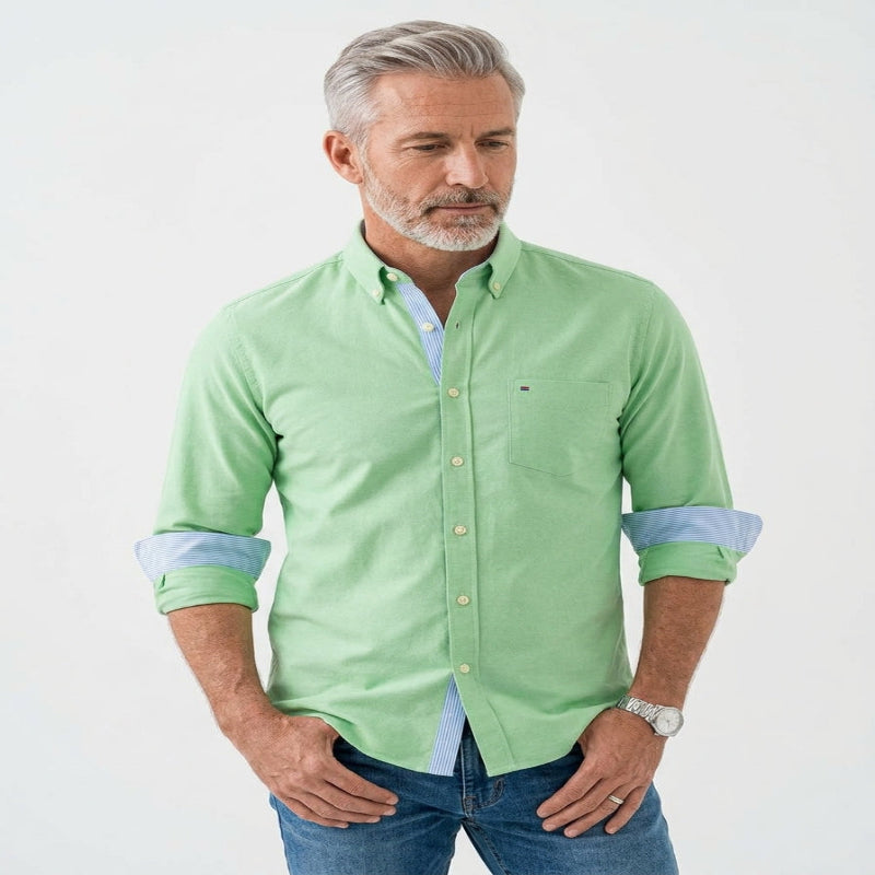 A man wearing a light green long-sleeve button-down shirt with light blue contrast inner placket and rolled-up sleeves, paired with blue jeans, against a plain white background. - Fashlot 
