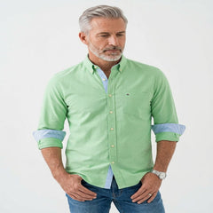 A man wearing a light green long-sleeve button-down shirt with light blue contrast inner placket and rolled-up sleeves, paired with blue jeans, against a plain white background. - Fashlot 