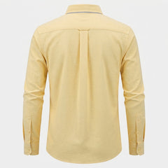 A pale yellow long-sleeve button-up shirt shown from the back, featuring a central pleat and button cuffs, displayed on a light gray background. - Fashlot