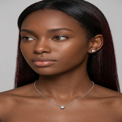 A close-up portrait of a woman with long dark hair wearing a delicate silver chain necklace with a small round clear stone pendant and a matching stud earring, against a plain light gray background. - Fashlot