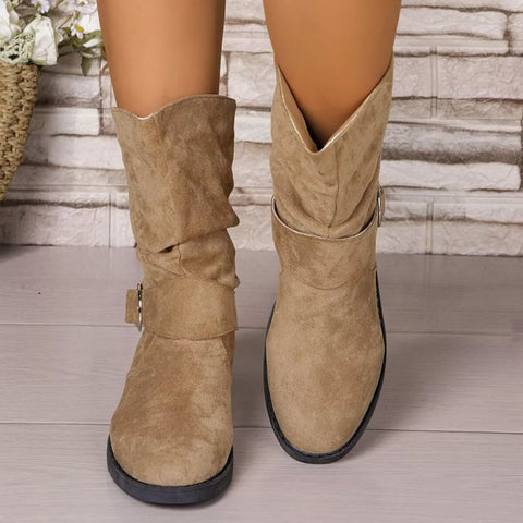 Beige suede boots worn by a person on a wooden floor with a stone wall background - Fashlot