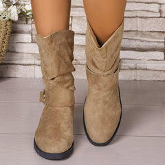 Beige suede boots worn by a person on a wooden floor with a stone wall background - Fashlot