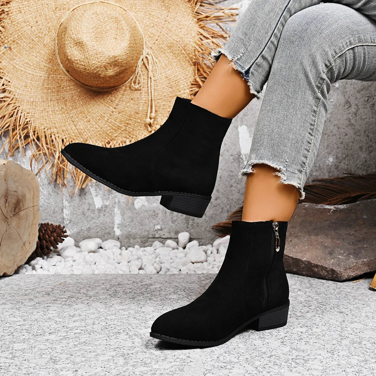 Person wearing black ankle boots with a straw hat and stones in the background - Fashlot