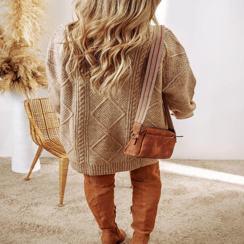 Person wearing a brown cable knit sweater and tan pants, holding a brown leather bag. Fashlot