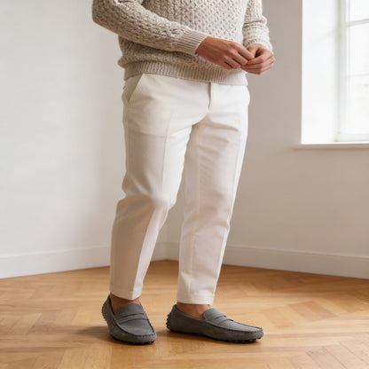 Person wearing a beige sweater, white pants, and gray shoes standing on a wooden floor.
