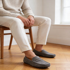 Person wearing gray loafers sitting on a wooden chair indoors.