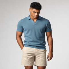 A man wearing a short-sleeve knit polo shirt in slate blue and beige shorts, standing against a light gray studio background. - Fashlot