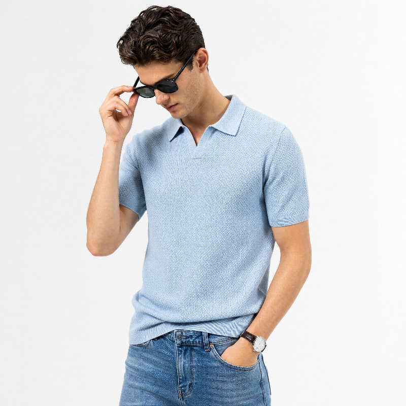 A man wearing a light blue short-sleeve polo shirt and blue jeans, posing against a plain white background while adjusting his black sunglasses. - Fashlot