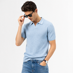 A man wearing a light blue short-sleeve polo shirt and blue jeans, posing against a plain white background while adjusting his black sunglasses. - Fashlot