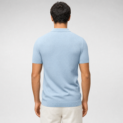 A man viewed from the back wearing a light blue short-sleeve knit polo shirt and off-white trousers, set against a neutral light gray studio background. - Fashlot