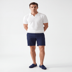 A man modeling a white short-sleeve polo shirt, navy blue shorts, and navy blue slip-on shoes against a plain white studio background. - Fashlot