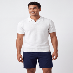 A man wearing a white short-sleeve polo shirt and navy blue shorts, standing against a light gray studio background. - Fashlot