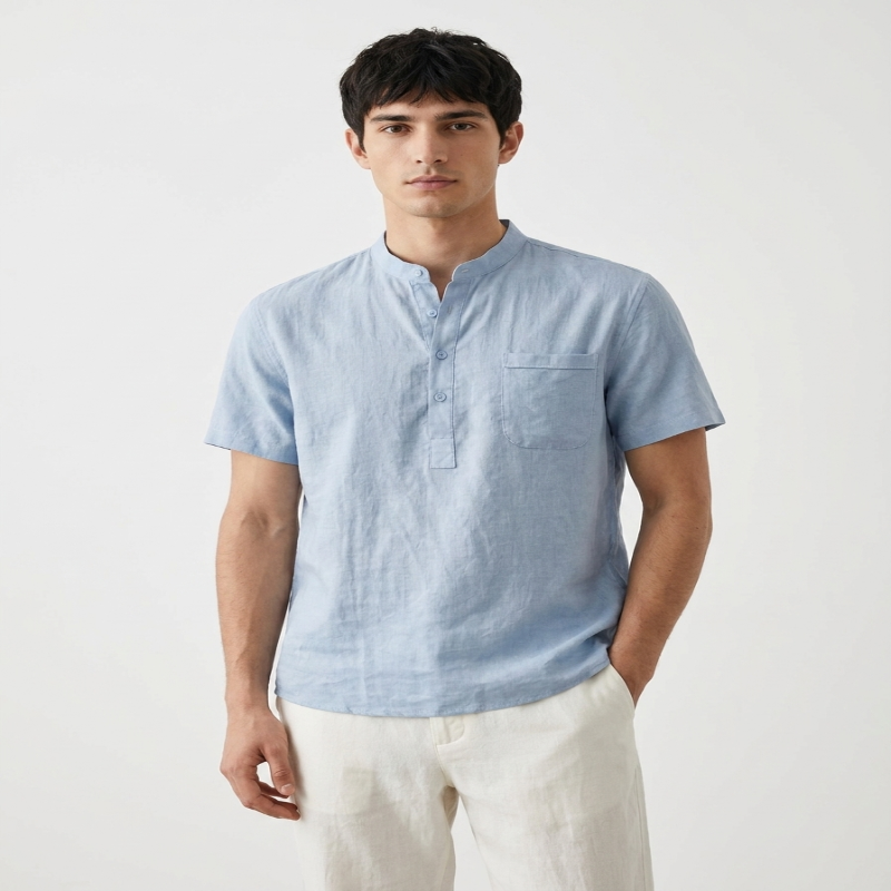 A man wearing a light blue short-sleeve linen shirt with a mandarin collar and white linen pants, standing against a plain white studio background. - Fashot