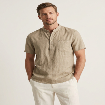 A man wearing a light beige linen short-sleeve henley shirt with white trousers, standing against a plain off-white studio background. - Fashlot
