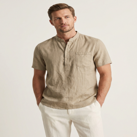 A man wearing a light beige linen short-sleeve henley shirt with white trousers, standing against a plain off-white studio background. - Fashlot