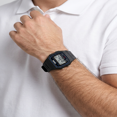 A black digital wristwatch with a blue bezel detail worn on a person's wrist, shown against a white polo shirt background. - Fashlot