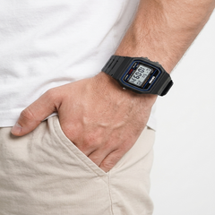 A close-up of a person's wrist wearing a black digital watch with a blue bezel detail, paired with a white t-shirt and beige pants. - Fashlot