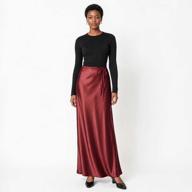 A black model stands against a white studio background wearing a black long-sleeve crewneck top and a high-waisted, floor-length satin midi skirt in a deep burgundy red. The skirt features a matching drawstring tie at the waist. - Fashlot