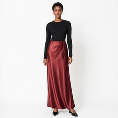 A black model stands against a white studio background wearing a black long-sleeve crewneck top and a high-waisted, floor-length satin midi skirt in a deep burgundy red. The skirt features a matching drawstring tie at the waist. - Fashlot